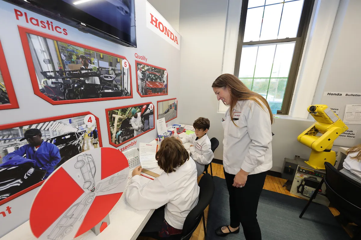Children sitting at a table with photos of auto manufacturing talking with a Honda employee