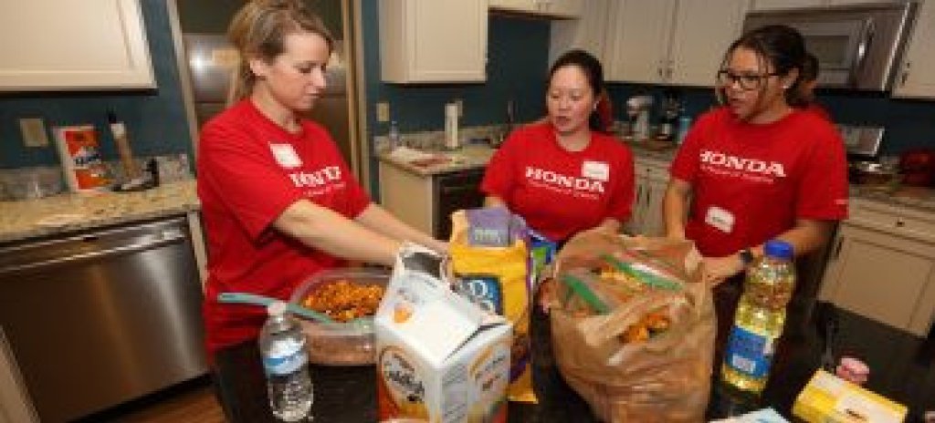 Three women wearing Honda shirts working in a kitchen.