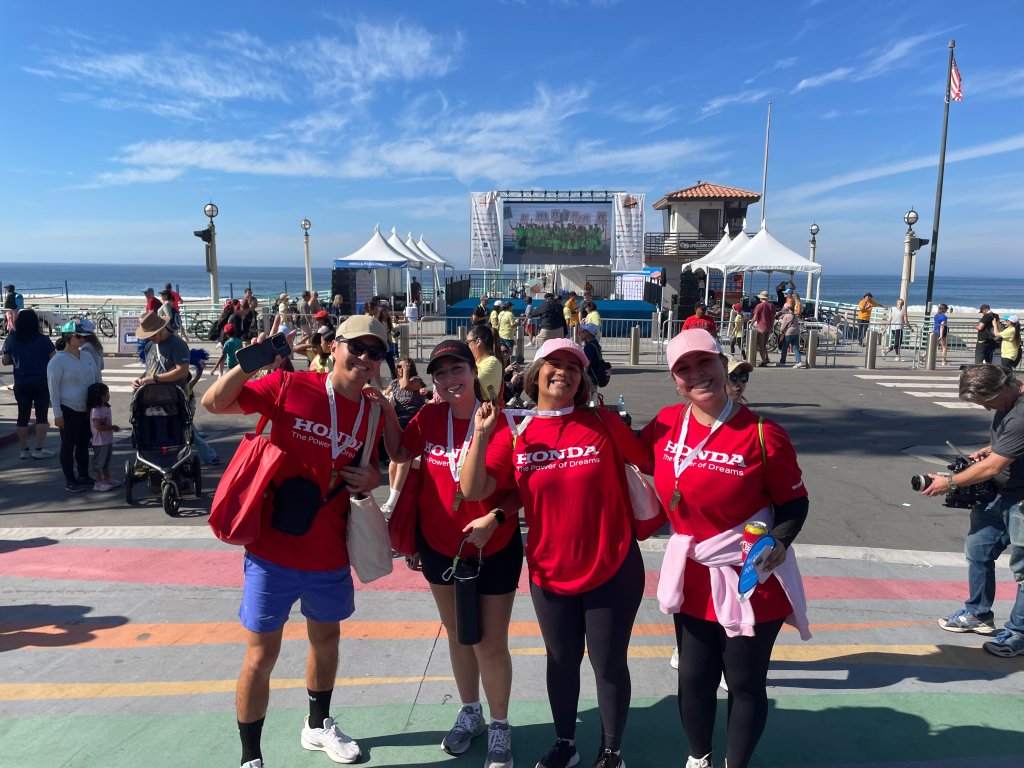 Four people wearing red Honda shirts pose with race medals at an outdoor event.