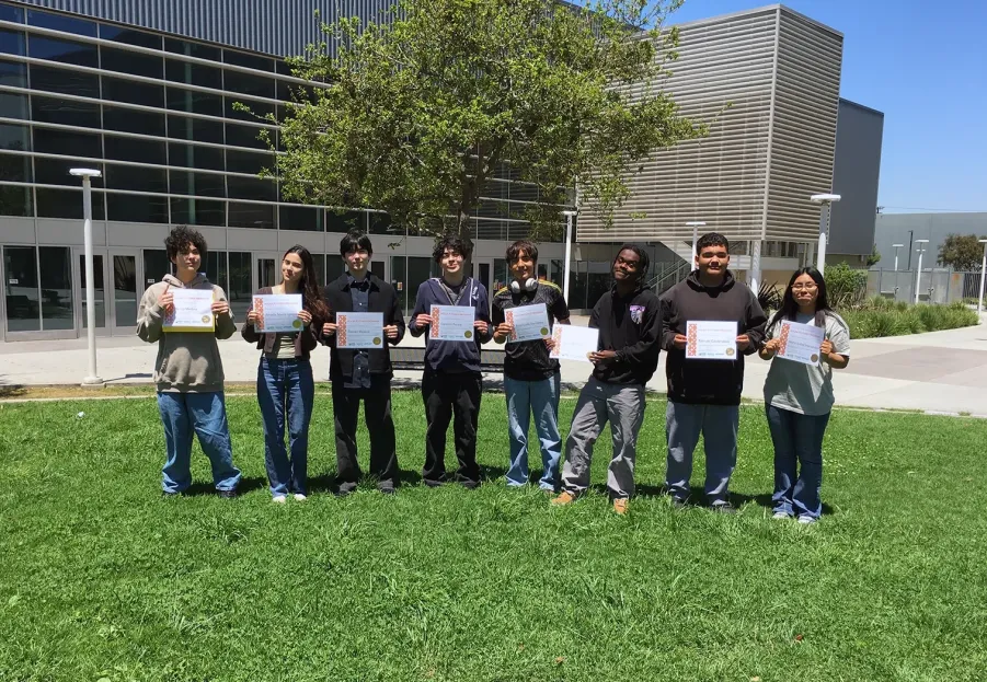 Students holding certificates in front of a building.