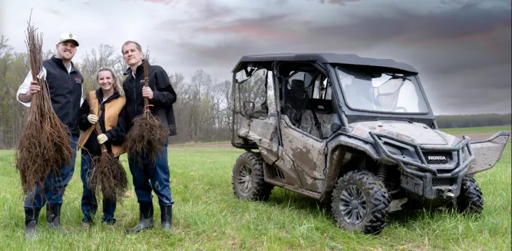 Three people holding tree branches next to a Honda ATV.