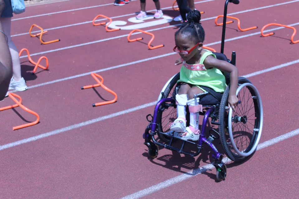 A little girl in a wheel chair on a race track.