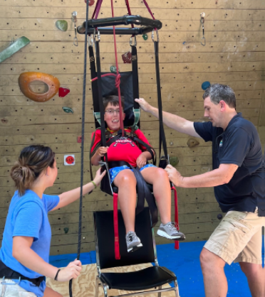 Two people helping another person in an adaptive mobility harness