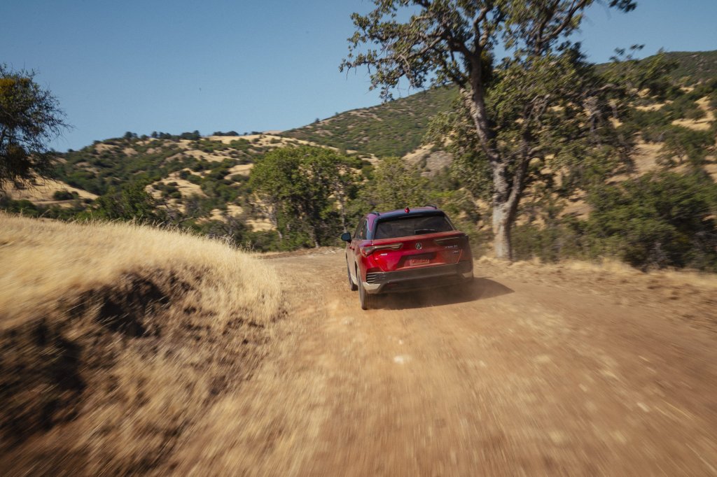 A back view of an Acura ZDX vehicle driving away on a dirt road in a scenic landscape.