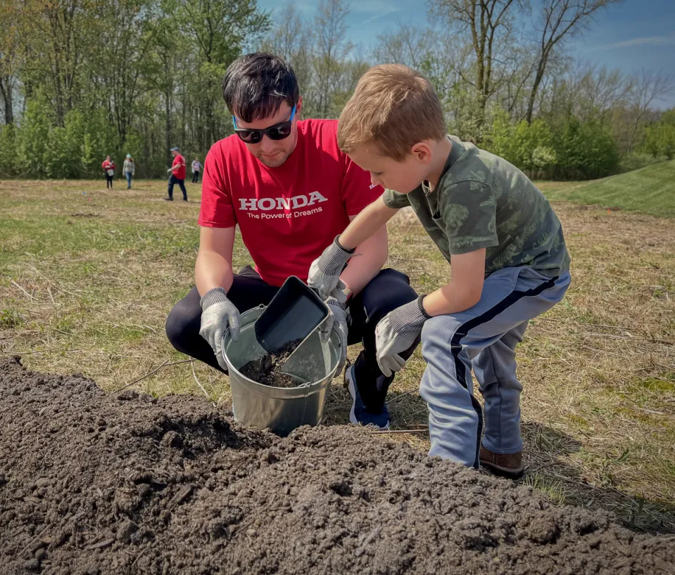 A volunteer and child filling a bucket with dirt.