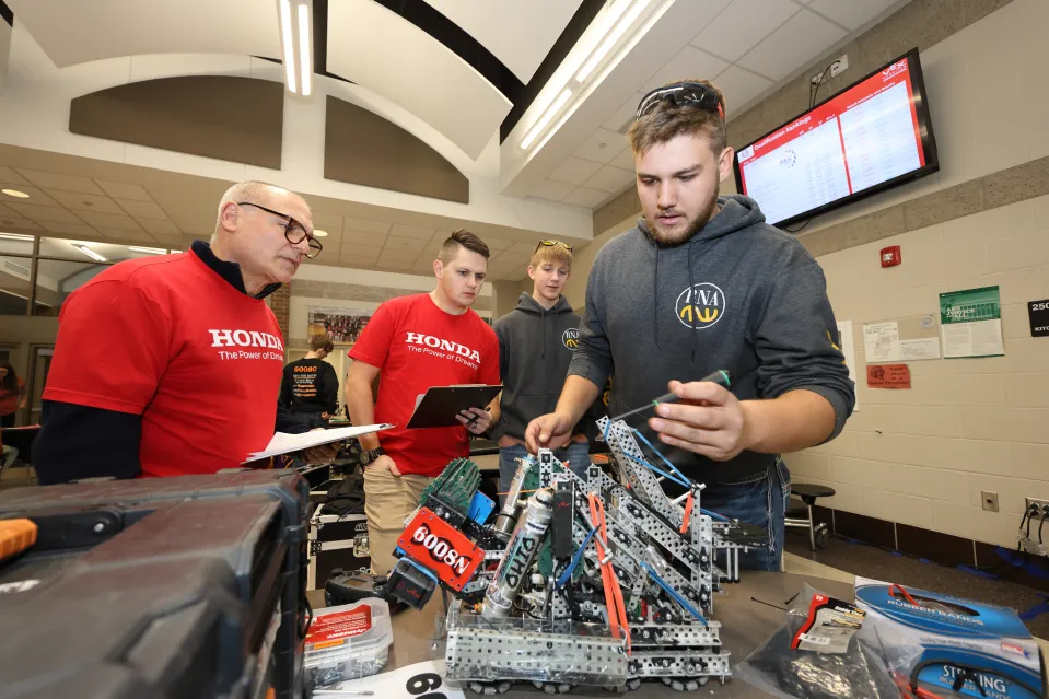 Two students show a metal robot to teachers.