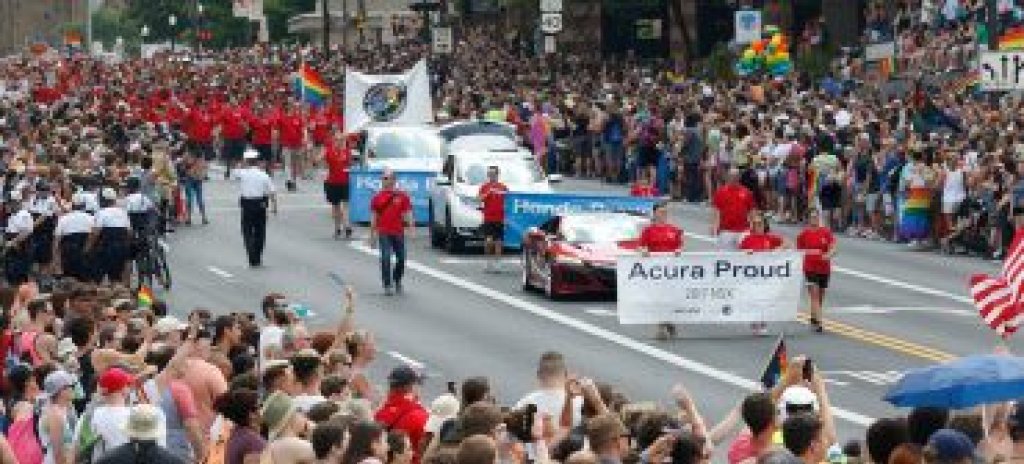People participating in a parade holding a banner with the text "Acura Proud".